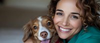 Happy young Caucasian woman with curly hair smiling while cuddling her adorable Australian Shepherd puppy at home. Pet ownership and companionship concept.
