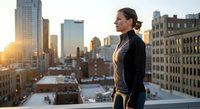 Professional businesswoman in elegant attire standing on urban rooftop at sunset with city skyline backdrop for corporate and lifestyle concepts.