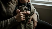 Tender moment of a mother holding her newborn baby wrapped in a soft blanket, capturing the bond of early parenthood and family love.