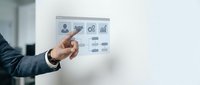 Male professional in dark business suit pointing at digital interface with user profile, settings, and analytics icons on transparent screen, representing software development, app design, and user experience management.