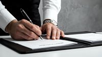 Professional businessman signing legal contract document with pen on clipboard at office desk for business agreement and partnership deal.