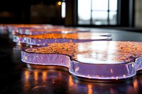 Glowing purple glass art installation with organic curved shapes creates dramatic lighting effect on dark surface, highlighting intricate etched patterns.