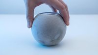 White round smart speaker held by a hand on a light background, showcasing modern wireless audio technology for home use.