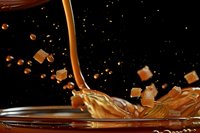 Liquid caramel pouring with sugar cubes splashing against black background. Sweet confectionery ingredient for desserts and candy making.