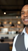 Confident African American male professional wearing gray vest and white shirt smiling in modern office environment with blurred background for corporate and business applications.