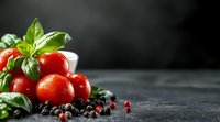 Fresh cherry tomatoes with water drops, green basil leaves and scattered peppercorns on dark stone background with copy space. Food photography.