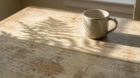 Rustic ceramic mug on weathered wooden table with natural sunlight casting shadows, creating warm, minimalist aesthetic for home decor and lifestyle content.