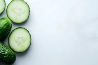 Fresh cucumber slices and whole green cucumber on white background, minimalist food composition with copy space for healthy eating concept.