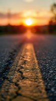 Road markings glowing in golden sunlight during sunset, with blurred horizon and warm sky creating atmospheric depth for travel and journey concepts.