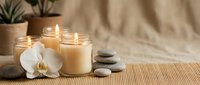 Glowing candles in glass jars with white orchid and stacked zen stones on bamboo mat, spa relaxation and wellness concept.