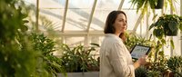 Young woman botanist with tablet studying tropical plants in modern greenhouse for research and agricultural technology applications.