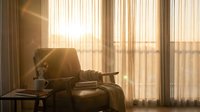 Cozy reading corner with open book and warm sunlight streaming through sheer curtains creating peaceful atmosphere for relaxation and literature enjoyment.