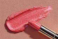 Shimmering pink lipstick swatch smeared on textured background with metallic tube, showcasing cosmetic product texture and application for beauty and makeup artistry.