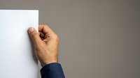 Mature male hand holding blank white paper against neutral gray background, suitable for business presentations, advertising mockups, and corporate communications.