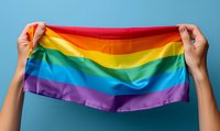 Hands holding up colorful rainbow pride flag against blue background, symbolizing LGBTQ+ community support, equality, and celebration of diversity.