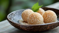 Traditional Asian sesame seed balls served on decorative ceramic plate with fresh green leaf garnish on wooden table surface for culinary presentation.