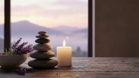 Zen spa stones balanced with burning candle and lavender flowers on wooden table overlooking serene mountain lake at sunset for wellness meditation.