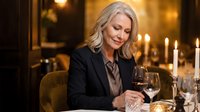Elegant mature blonde businesswoman enjoying wine at upscale restaurant with candlelight ambiance for luxury dining and professional lifestyle content.