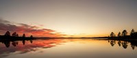 Serene lake at sunset with golden and orange sky reflecting on calm water surface, silhouetted trees along shoreline, peaceful nature landscape for relaxation and meditation projects.