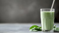 Fresh green smoothie with spinach leaves and straw in tall glass on gray background, healthy breakfast drink with copy space for wellness content.