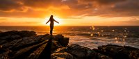 Silhouetted figure standing on rocky coastline with arms outstretched during golden sunset, waves crashing below, conveying freedom and achievement for motivational and lifestyle content.