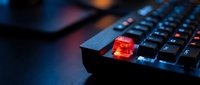 Red illuminated escape key on black gaming keyboard with colorful RGB lighting in dark environment for technology and computer concepts.