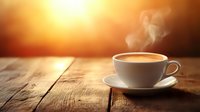 Hot coffee cup with rising steam on rustic wooden table against warm golden sunrise background, creating cozy morning atmosphere with dramatic lighting.