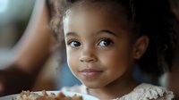 Young African American girl with curly hair smiling at camera in soft natural lighting. Child portrait photography for family and lifestyle content.
