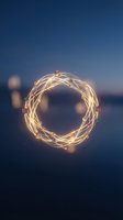 Glowing string lights arranged in circular shape against twilight sky with blurred bokeh background, suitable for festive, holiday, and celebration design projects.