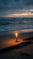 Burning candle on sandy beach at sunset with ocean waves and dramatic cloudy sky creating peaceful romantic atmosphere for meditation and relaxation.