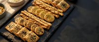 Freshly baked breadsticks with sesame seeds arranged on dark slate board, perfect for bakery, food photography, culinary blogs, restaurant menus and cooking publications.