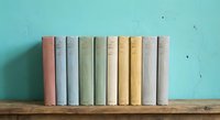 Row of vintage books with pastel colored spines arranged on wooden shelf against turquoise wall for home decor and reading concepts.
