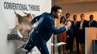 Professional businessman breaking through paper barrier with conventional thinking text during corporate presentation to audience.