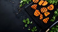 Grilled sweet potato slices with char marks on black cast iron grill pan, garnished with fresh parsley and peppercorns on dark background, food photography.