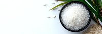 White jasmine rice grains in black ceramic bowl with green palm leaf on light background, top view composition for Asian cuisine and food design.