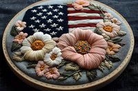 Patriotic embroidery hoop featuring American flag with blooming flowers in pink and coral tones. Handcrafted needlework art for Independence Day decor.