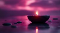 Burning candle in stone bowl creates peaceful ambiance with purple pink sunset sky reflecting on calm water surface surrounded by smooth pebbles for meditation.
