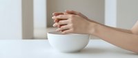 Female hands cupping around white ceramic bowl on clean table surface in minimalist interior setting for wellness and self-care concepts.