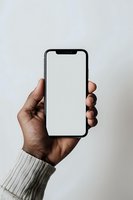 Hand holding smartphone with blank white screen mockup for app presentation and mobile interface design against neutral background.