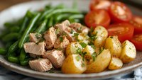 Nutritious plate with sliced roasted meat, baby potatoes, green beans, and cherry tomatoes garnished with fresh herbs.