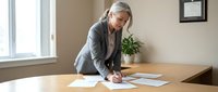 Senior businesswoman with gray hair reviewing documents at office desk, professional corporate environment for business presentations.