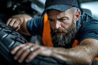 Focused Caucasian auto mechanic with gray beard wearing cap inspects tire tread during routine maintenance service at professional garage workshop.