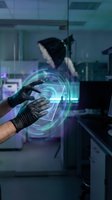 Scientist wearing black gloves manipulating glowing holographic data interface in modern laboratory setting with colleague in background, representing digital innovation and technology research.