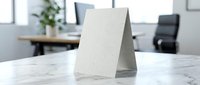 Blank white paper tent card mockup on marble desk in modern office workspace for menu display, table signage, promotional materials and business presentations.