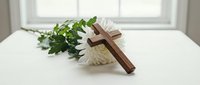 Wooden cross with white flowers on table for funeral memorial service, religious ceremony, sympathy condolences, spiritual comfort and remembrance.