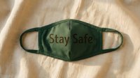 Green fabric face mask with Stay Safe text lying on beige linen background, health protection and safety awareness concept.