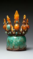Ornate ceremonial crown featuring amber-colored spires and turquoise gemstones set against patinated copper base, photographed on dark background with dramatic lighting.