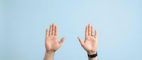 Two hands raised up showing palms in stop gesture or greeting sign against light blue background for communication and body language concepts.