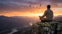 Man meditating on mountain peak at sunset with flying birds and valley view below, peaceful mindfulness and spiritual wellness concept for relaxation.