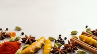 Aromatic spices and herbs border with turmeric, cinnamon, star anise, cardamom and paprika on neutral background for culinary design projects.